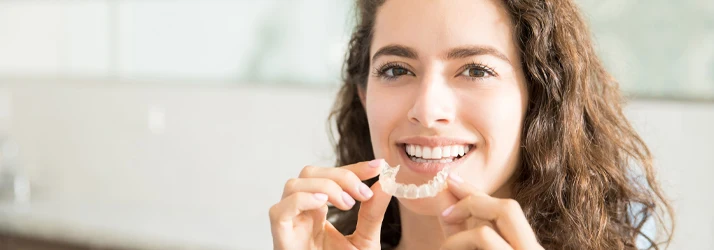 Orthodontist Orlando FL Invisalign Focused A woman is smiling, holding her Invisalign device about to put it in