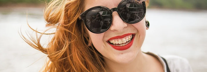 Orthodontist Orlando FL Retainers Focused A woman on the water wearing sunglasses is smiling wide showing her retainer
